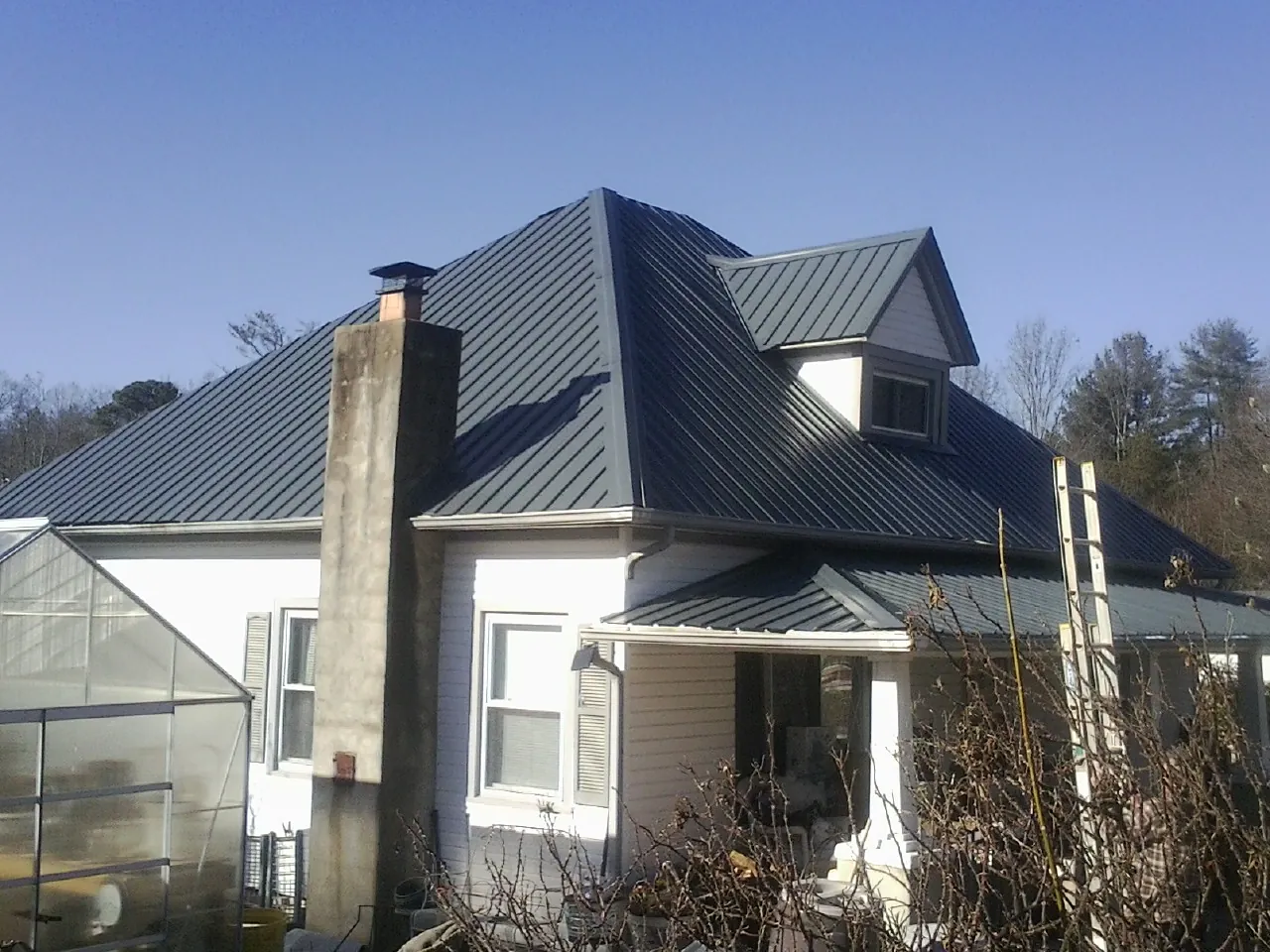 Dark blue standing seam metal roof on a white farmhouse with dormer — Slate & Tile Roof Repair by Roofing Brothers in Forest Lakes