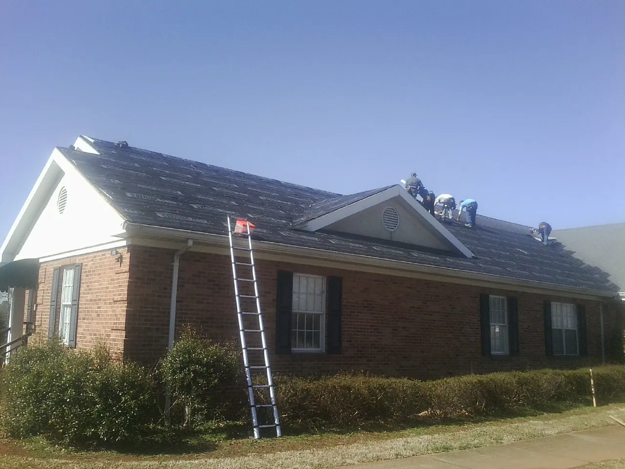 Crew tearing shingles off a brick ranch roof with a ladder set — Emergency Roof Repair work by our crew in Forest Lakes