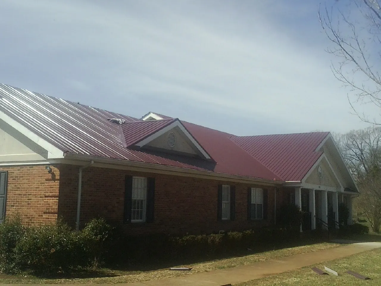 Red metal roof with gabled entries on a long brick building, from a Hail Damage Roof Repair job in Forest Lakes