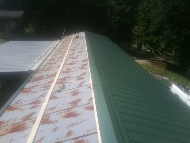 Old rusted panels beside newly installed green metal roofing in Forest Lakes