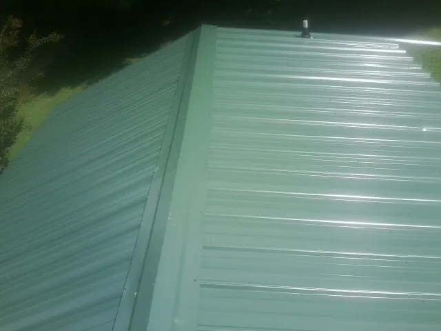 New green metal panels meeting at the ridge of a roof — Flat Roof Repair work by our crew in Forest Lakes