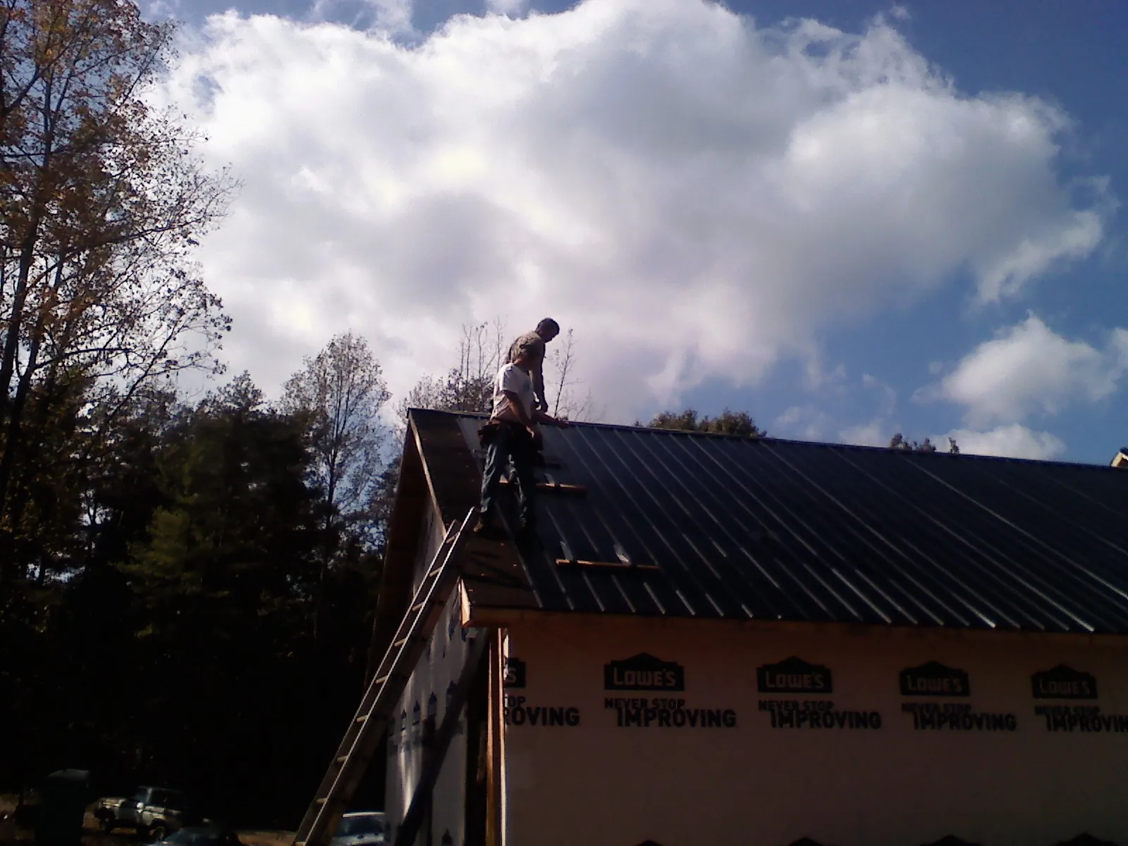 Roofer fastening dark metal panels high against a cloudy sky, from a Roof Inspection job in Forest Lakes