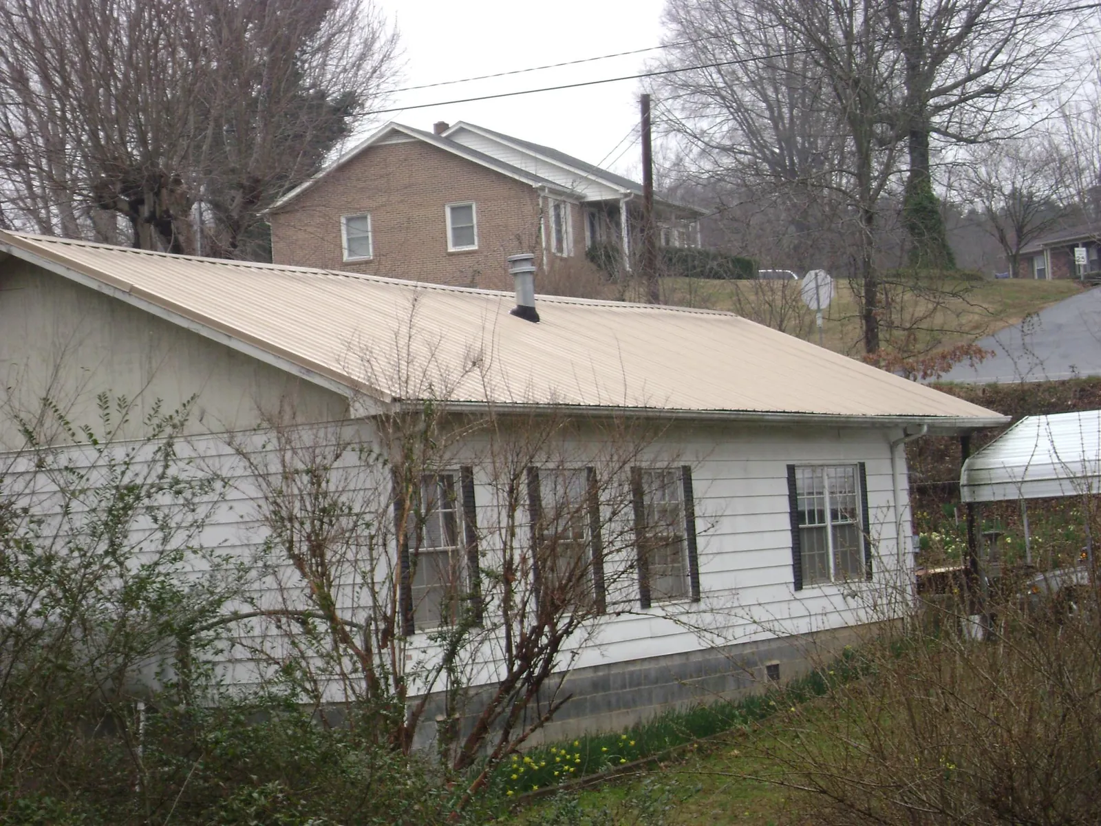 Tan metal roof on a white sided house set into a hillside — Commercial Roofing by Roofing Brothers in Forest Lakes