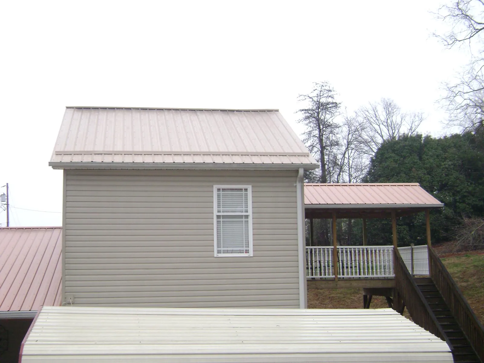 Tan metal roofs on a two story addition and attached porch, from a Roof Replacement job in Forest Lakes
